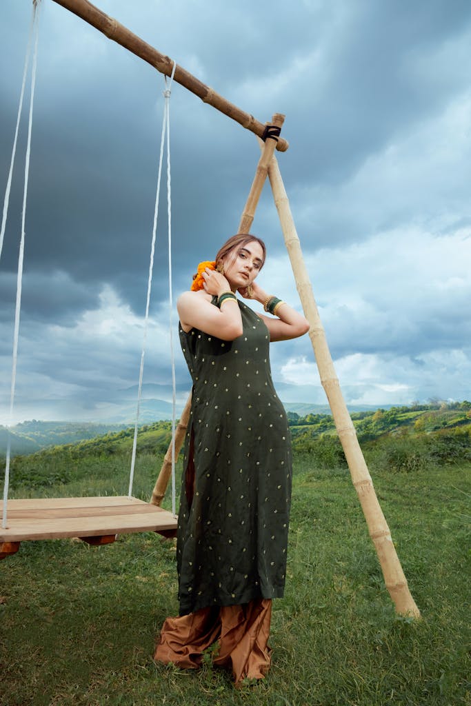 A woman in traditional attire poses by a wooden swing against a scenic outdoor backdrop.
