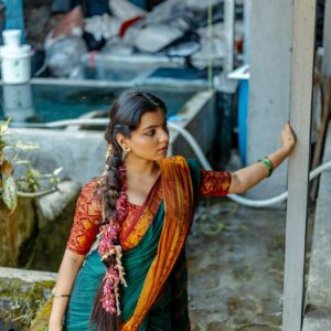 A woman in a colorful saree poses outdoors, showcasing traditional attire in a natural setting.