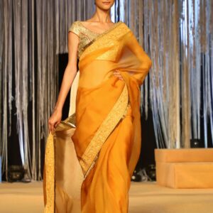 Model in a yellow saree walks the ramp at an indoor fashion event in India.